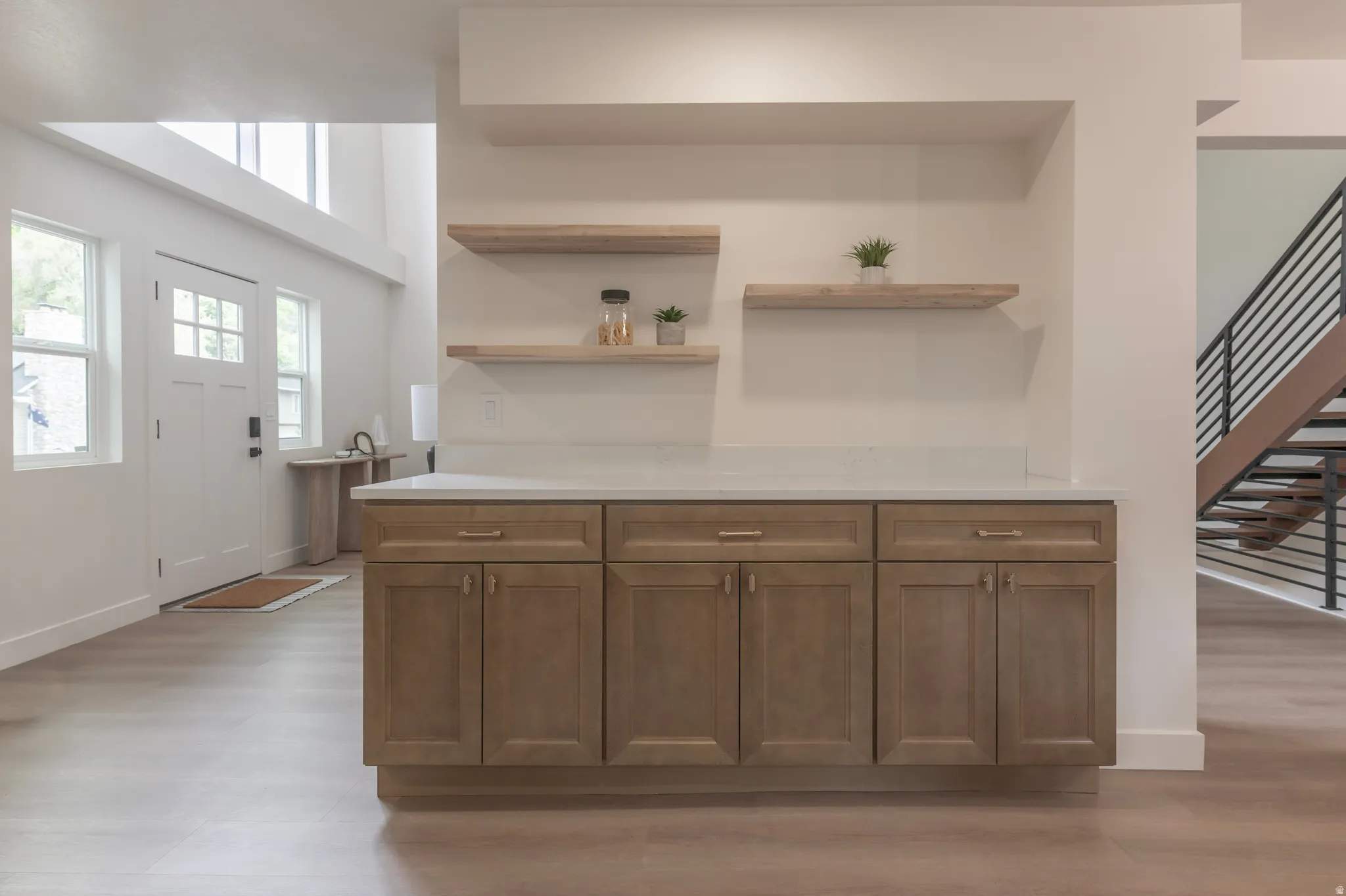 Warm wood-finish cabinetry with gold-tone hardware, white countertop, and floating wood-finish shelving