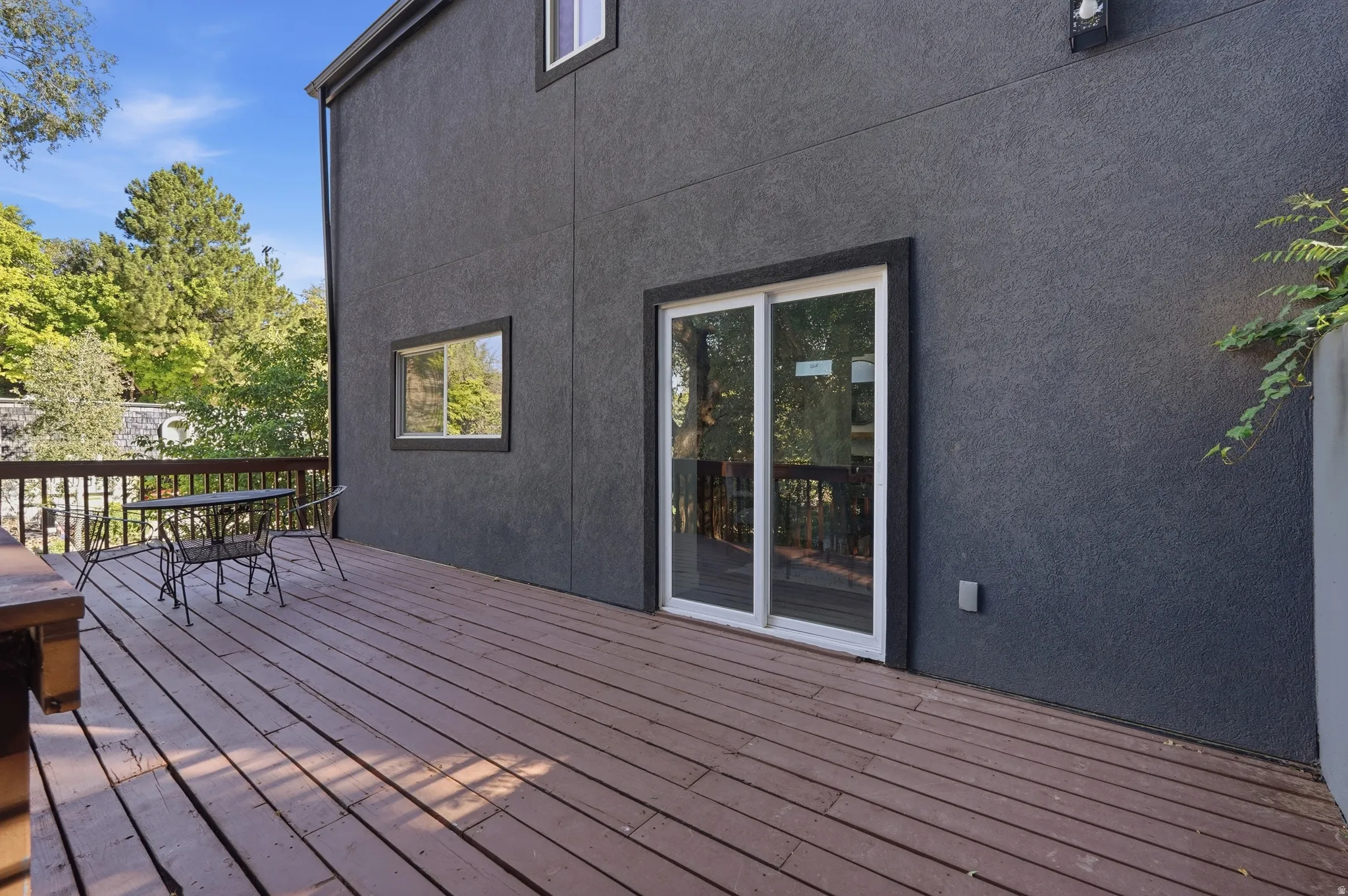 Expansive wood-plank deck with railing, featuring a sliding glass door and a rectangular window