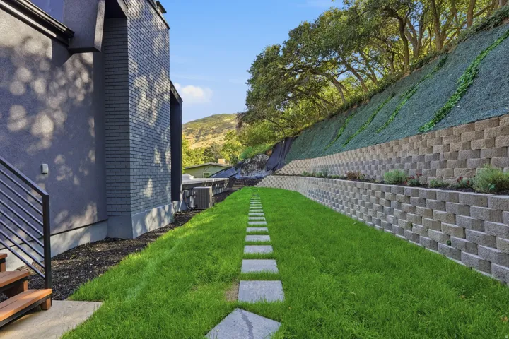 Manicured lawn with stepping stones, tiered retaining walls, and established upper-level landscaping