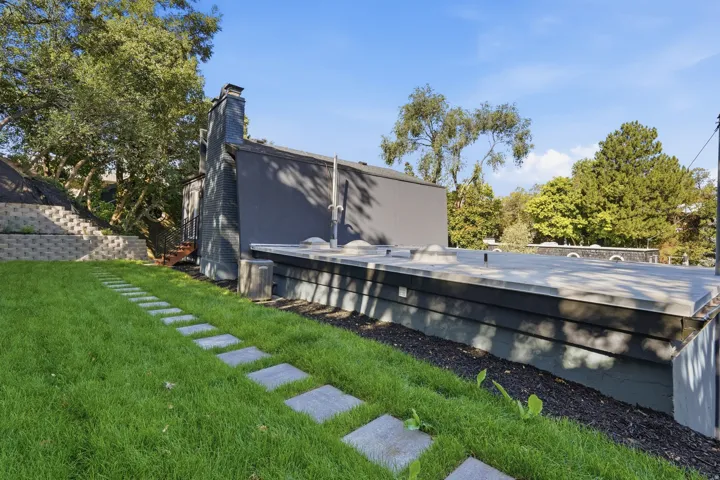 Expansive green lawn with stepping stone pathway, tiered retaining wall, and a rooftop deck