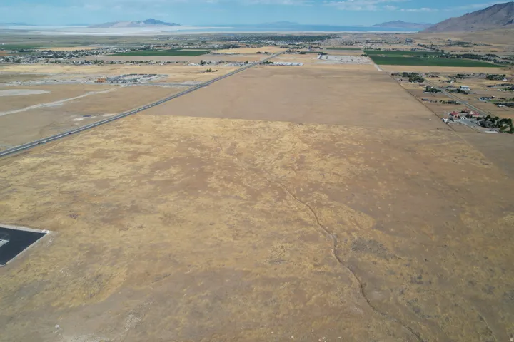 Expansive undeveloped land with a distant body of water, mountains, and a paved road
