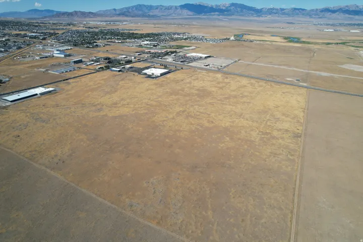 Expansive undeveloped land featuring a clear perimeter, distant commercial structures, and a mountain backdrop