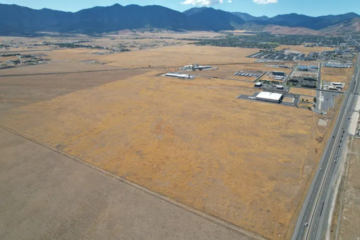 Expansive land parcel with direct highway frontage, featuring commercial structures and residential areas in the background, all set against a prominent mountain range
