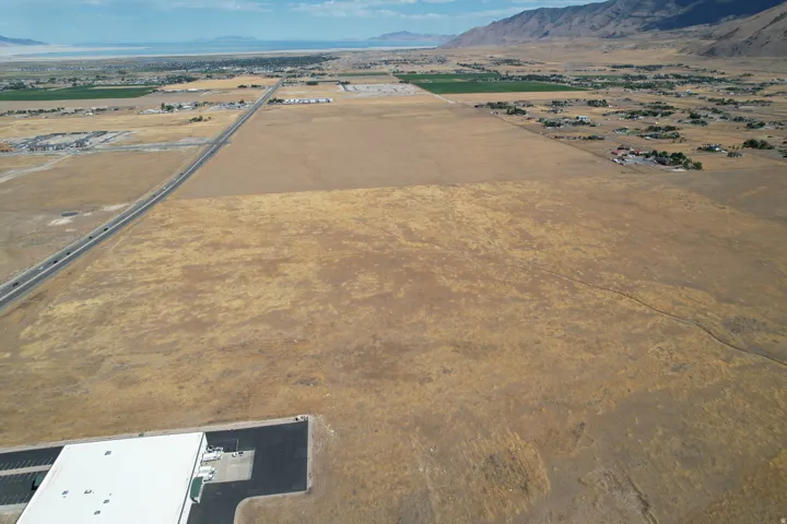 Expansive land parcel featuring a large commercial building, adjacent paved highway access, and distant mountain and water features