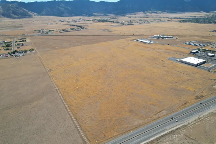 Expansive undeveloped land featuring a highway frontage, mountain backdrop, and surrounding commercial structures