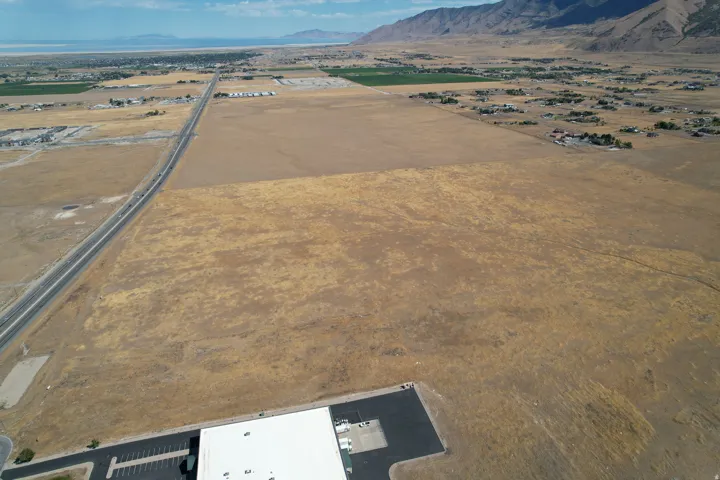 Expansive undeveloped land with a distant body of water, bordered by mountains, adjacent to a paved road, and a commercial building