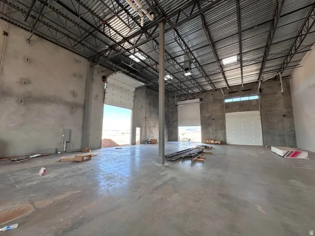 Spacious commercial interior featuring a high exposed ceiling with metal trusses, concrete flooring, and multiple roll-up doors