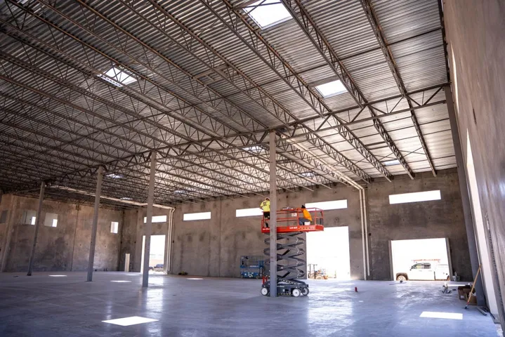 Expansive interior with exposed metal truss ceiling, multiple skylights, concrete flooring, and multiple openings