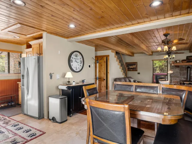 Open-concept kitchen and dining area featuring wood-beam cathedral ceiling with recessed lighting, stainless steel refrigerator, wood-finish dining table with seating for six, and tile flooring throughout the main living space