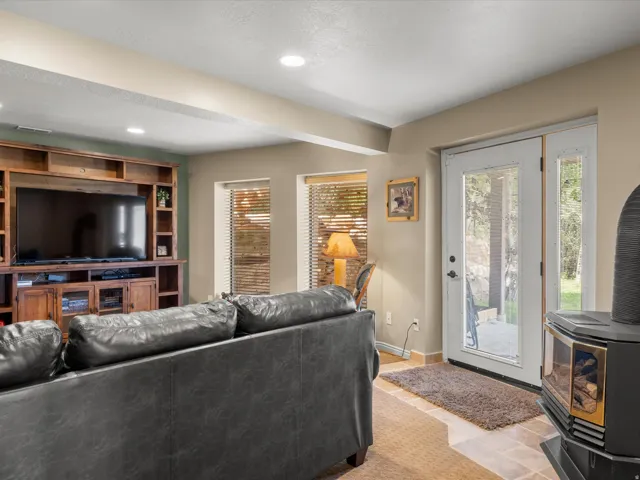 Recessed lighting throughout the ceiling, built-in entertainment center, two windows with blinds, glass-paneled exterior door, and a freestanding fireplace