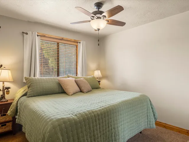 Ceiling fan with light fixture, window with wood-finish blinds, light-colored wall paint, and textured ceiling