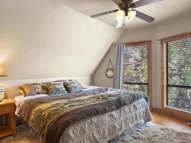 Vaulted ceiling with a ceiling fan, dual large windows with natural wood trim, and wood-finish flooring