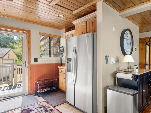 Wood-finish plank ceiling, stainless steel refrigerator, wood-finish cabinetry, and a glass-paneled exterior door leading to a deck