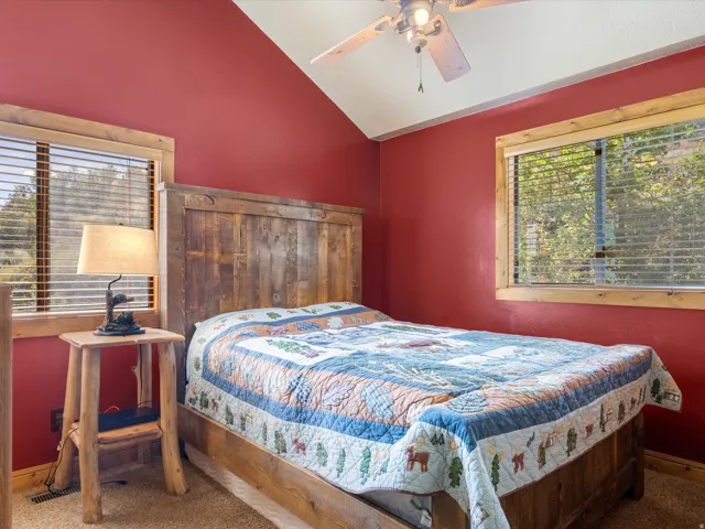 Vaulted ceiling with a ceiling fan, dual windows with wood trim, and textured wall finish