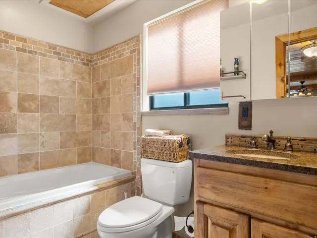 Built-in bathtub with subway tile surround, wood-finish vanity with stone countertop, and integrated sink