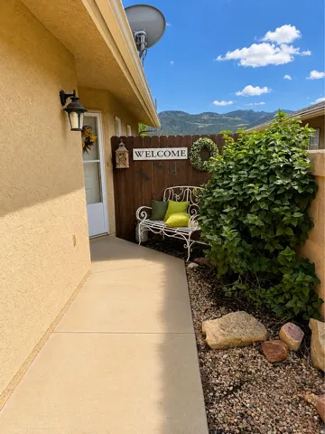 Concrete walkway leading to an entry door, bordered by a gravel and rock landscaping feature and a wooden privacy fence