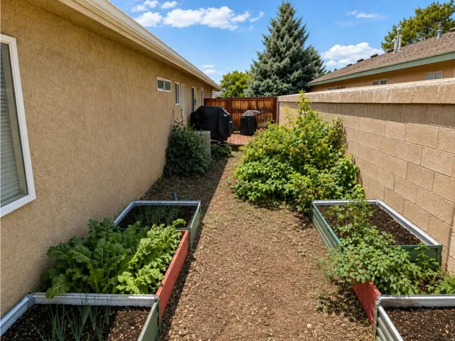 Side yard with raised garden beds, stucco exterior, privacy fencing, and mature landscaping