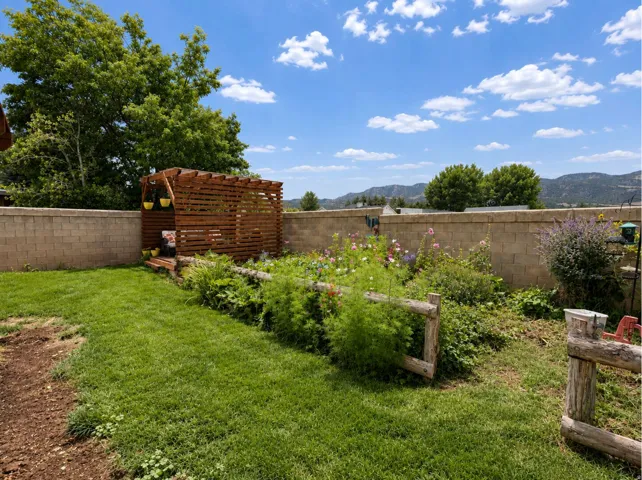 Expansive backyard featuring a manicured lawn, a wooden pergola, and a raised garden bed with a split-rail fence
