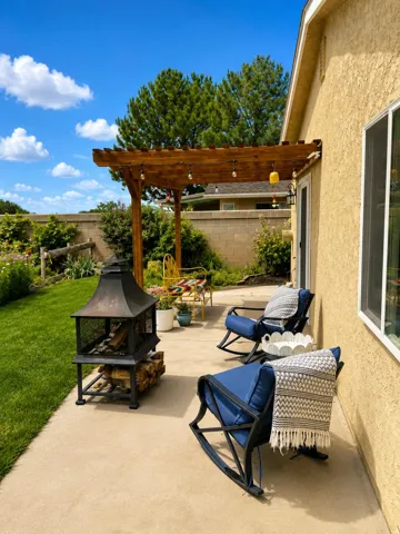 Paved patio featuring a wood pergola with integrated lighting, a built-in fire pit, and a manicured lawn area