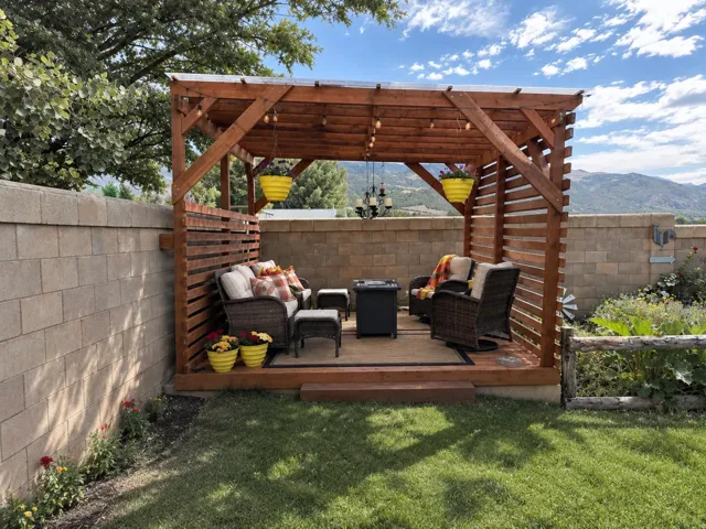 Wooden pergola with a slatted privacy screen, elevated wooden deck, string lighting, and a chandelier fixture