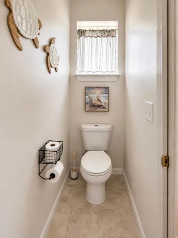 Tiled flooring, white toilet, and a window with a white frame