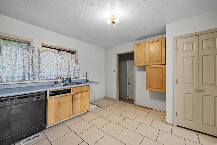 Tile flooring, wood cabinetry, dual windows, integrated sink, and a black dishwasher