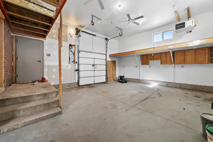 Concrete flooring, overhead garage door, built-in cabinetry, upper transom window, and dual ceiling fans