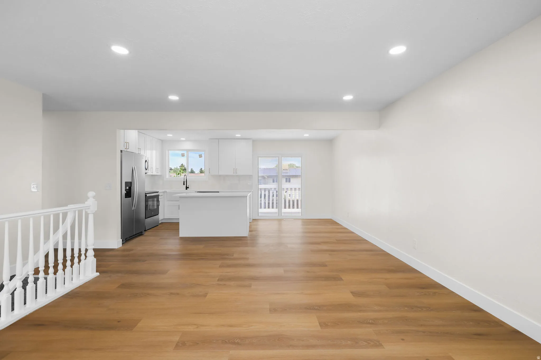 Open-concept living area with wood-finish flooring, recessed lighting, and a white balustrade