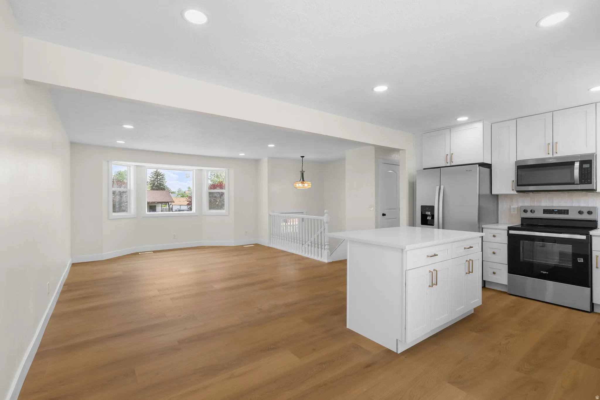 Open-concept living space with wood-finish flooring, recessed lighting, and a kitchen featuring white cabinetry, stainless steel appliances, and a central island with a solid surface countertop