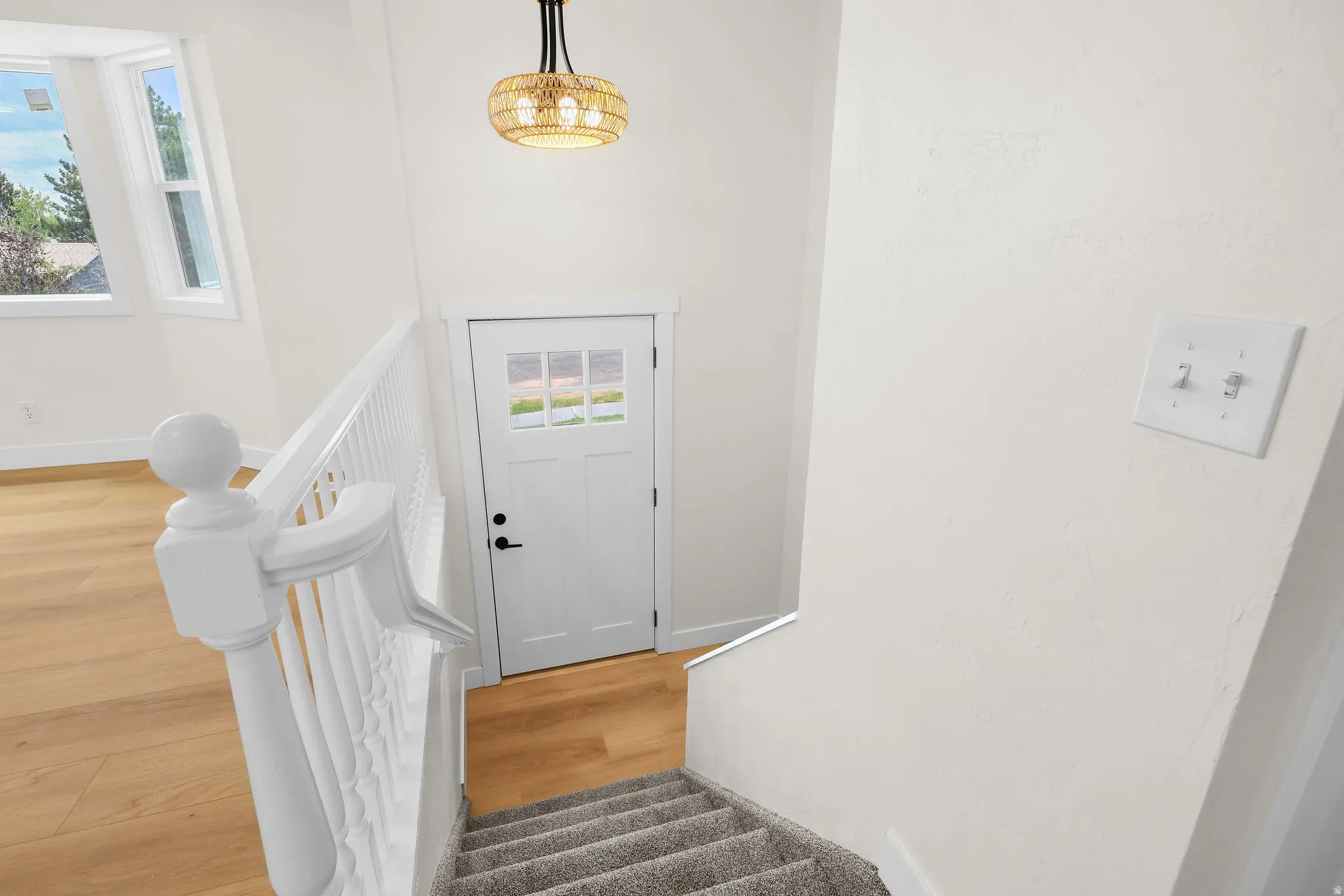 White painted wood handrail, carpeted stairs, and wood-finish flooring
