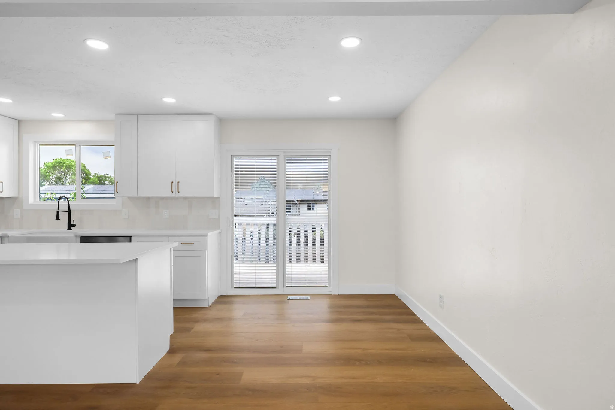 Kitchen island with a solid surface countertop, wood-finish flooring, white cabinetry, a black gooseneck faucet, and a sliding glass door to an outdoor deck