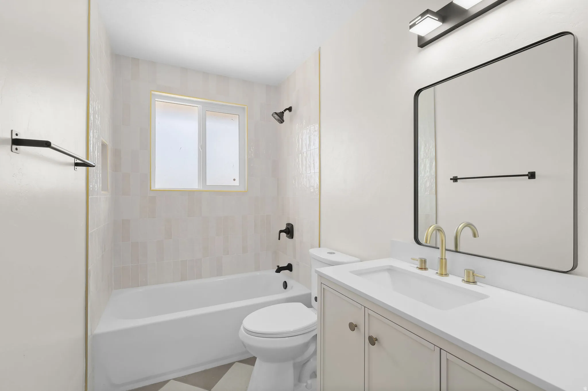 Built-in bathtub with subway tile surround, vanity with an integrated sink and gold-finish fixtures, and a rectangular frameless mirror with a black border