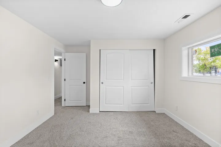 Light-colored carpeted flooring, white walls, white trim, sliding closet doors, and an overhead flush-mount light fixture