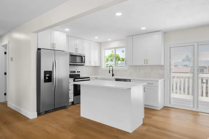 Kitchen featuring white cabinetry, stainless steel appliances, a center island, wood-finish flooring, and a sliding glass door leading to an outdoor deck