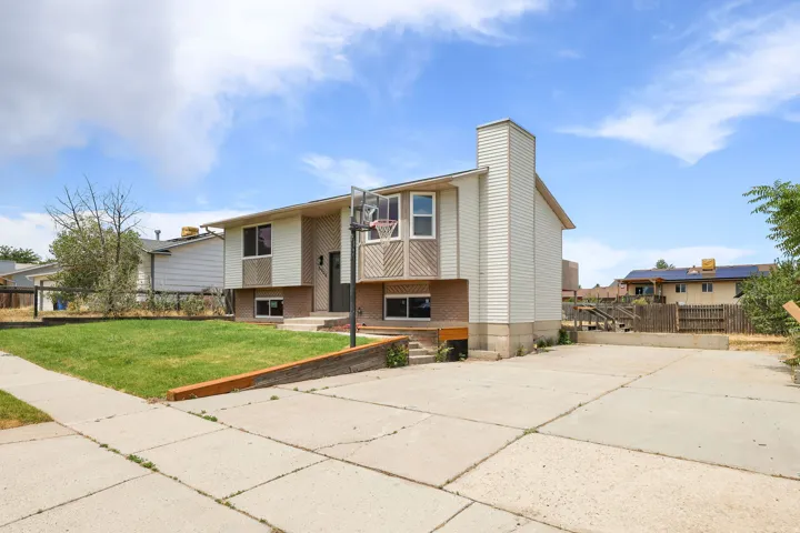 Split-level residence featuring a prominent chimney, concrete driveway, and a front lawn with a retaining wall
