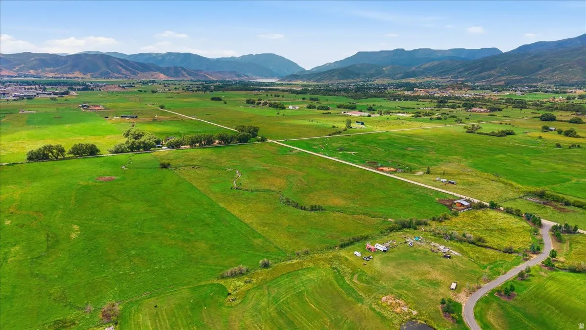 Expansive green fields with distant mountains and a body of water under a clear sky
