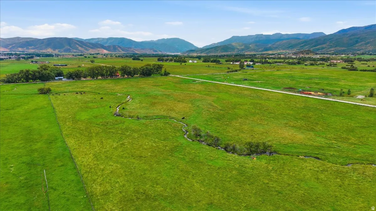 Expansive green fields with a winding stream, bordered by distant mountains