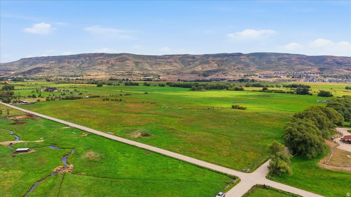 Expansive green acreage featuring a defined road, a natural stream, and distant mountain backdrops