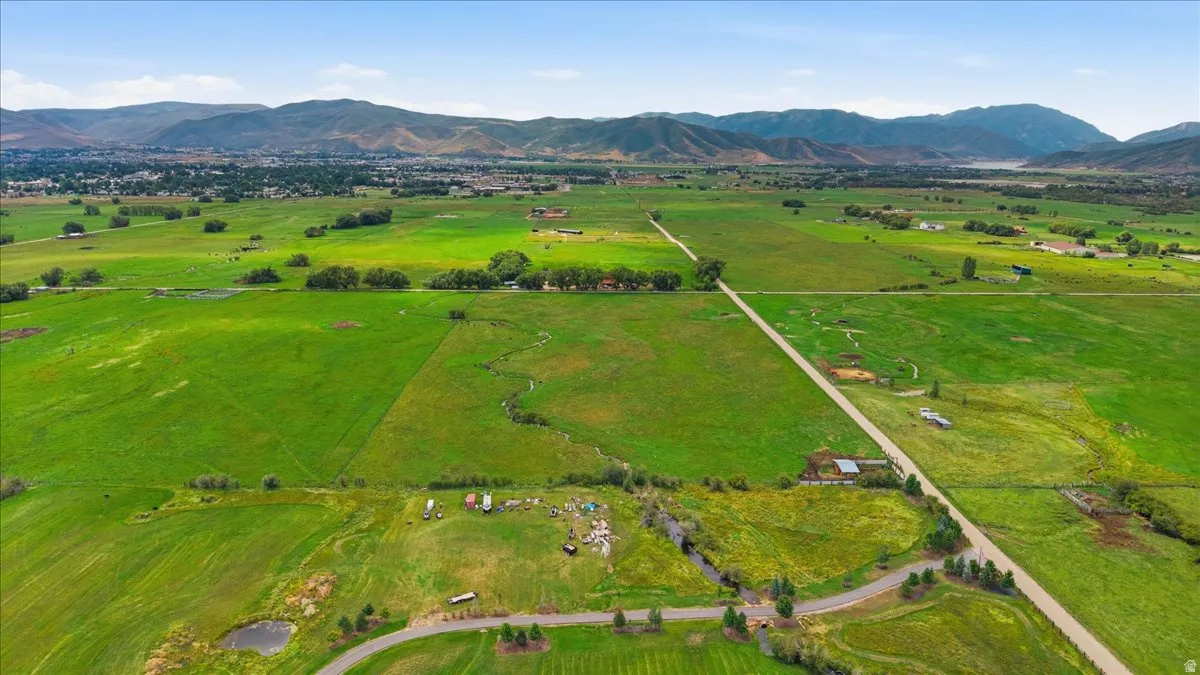 Expansive green fields with a winding stream, distant mountains, and a clear sky overhead