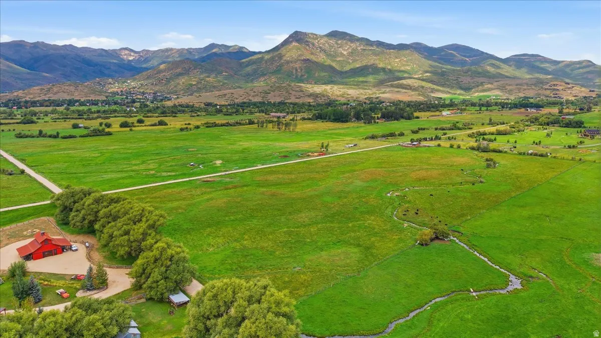 Expansive green pastures with a meandering stream, featuring a red barn structure and distant mountain ranges