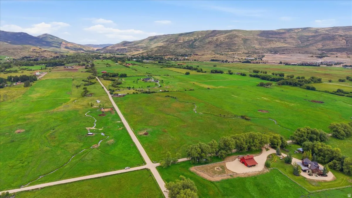 Expansive green landscape with distant mountains, featuring a red barn-style structure and an additional residential property