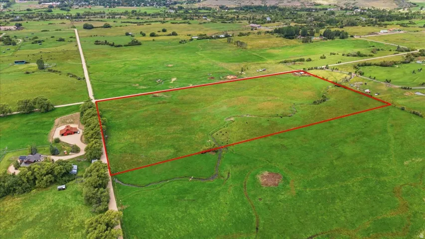 Expansive green acreage outlined by a red boundary, featuring a winding stream and a visible dirt road