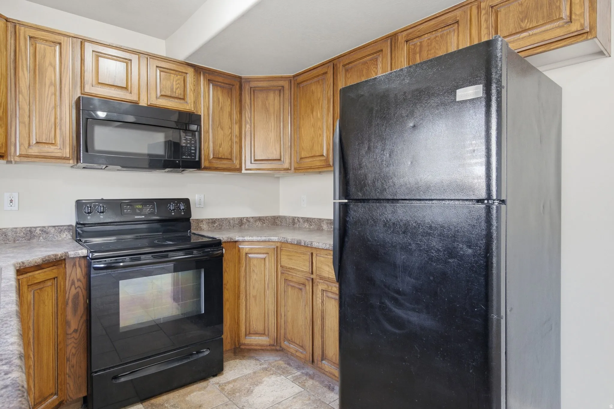 Kitchen featuring wood cabinetry, laminate countertops, black electric range, black microwave, and black refrigerator