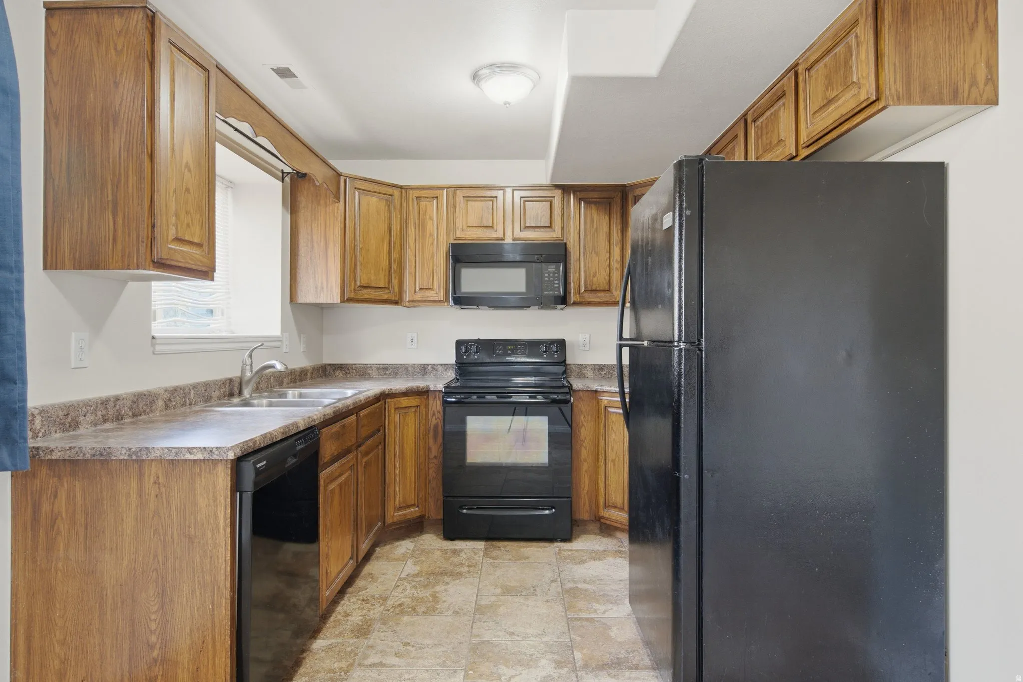 Kitchen with wood-finish cabinetry, laminate countertops, a double basin stainless steel sink, and tile flooring