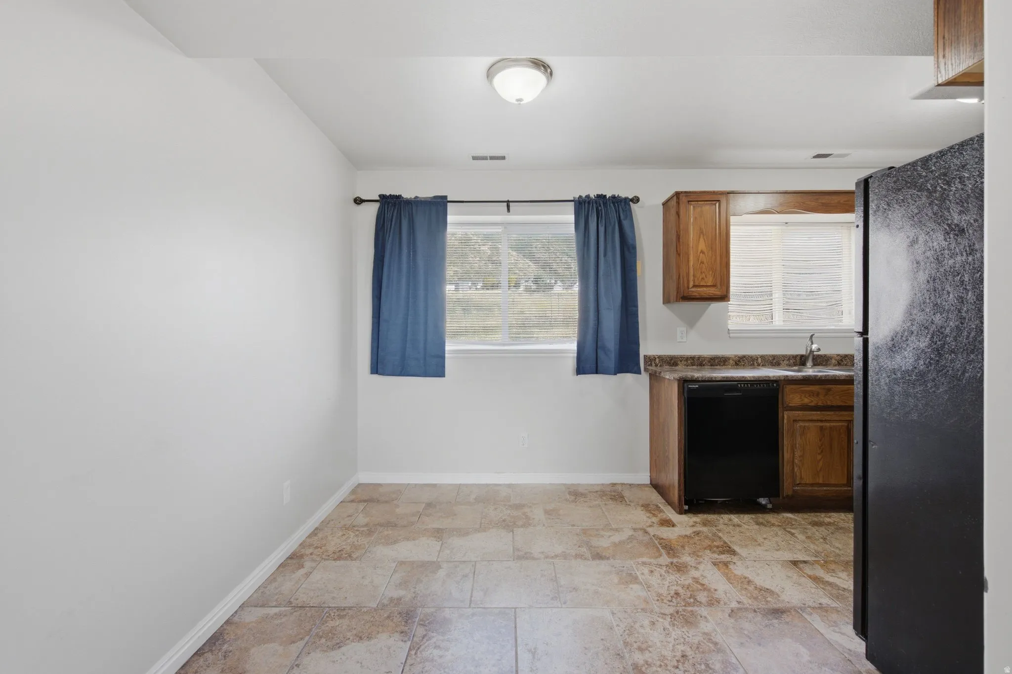 Kitchenette featuring wood-finish cabinetry, a black dishwasher, and a stainless steel sink