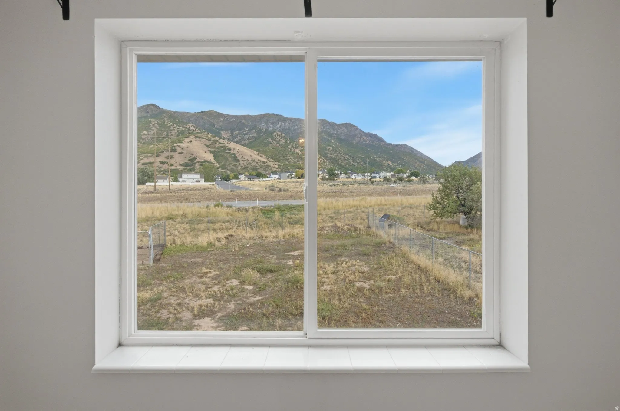 White-framed window with a wide sill, offering expansive scenery of distant mountains, a vast open field, and scattered residential structures