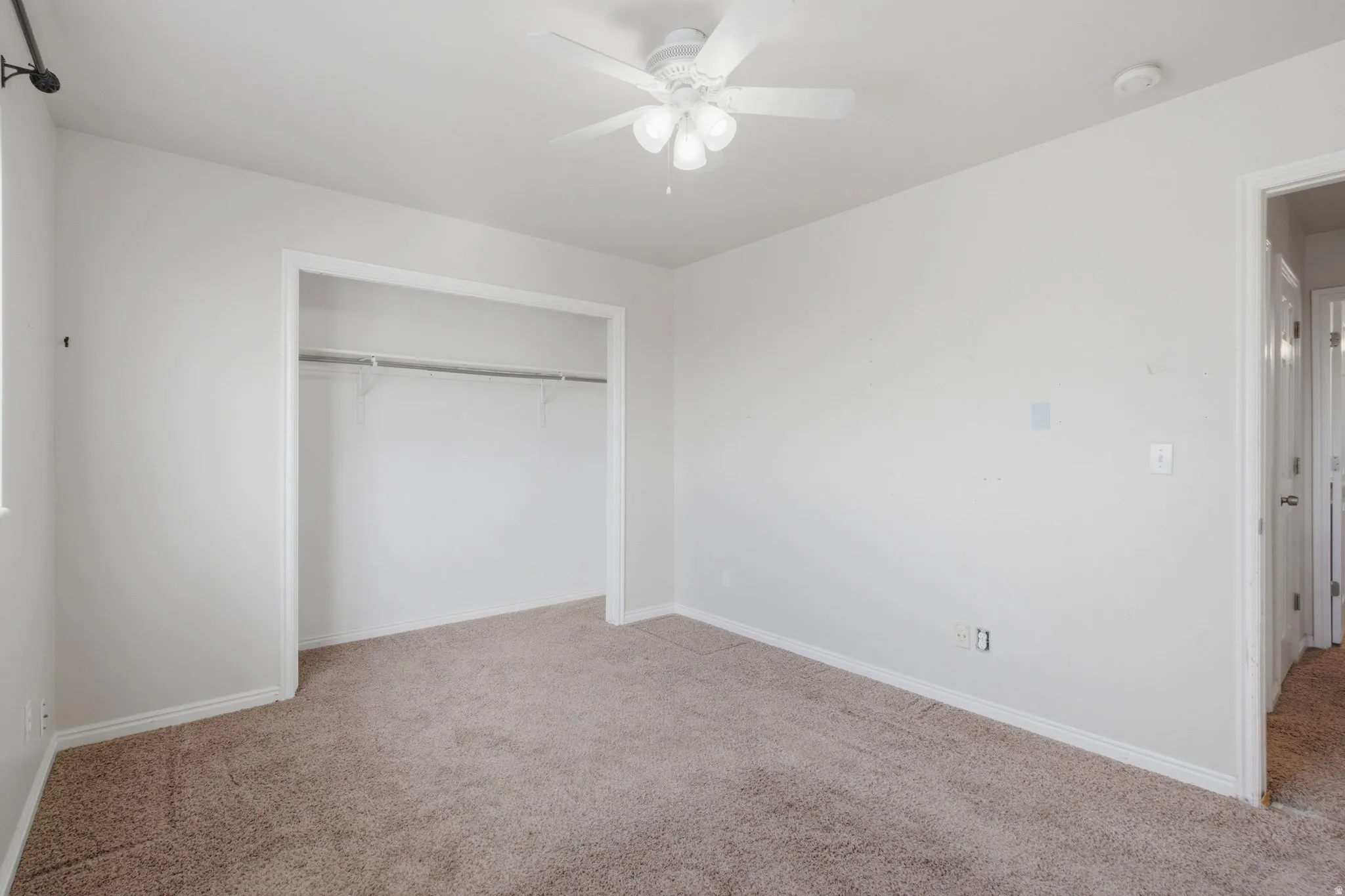 Neutral-toned carpeting, white walls, and a ceiling fan with light fixture