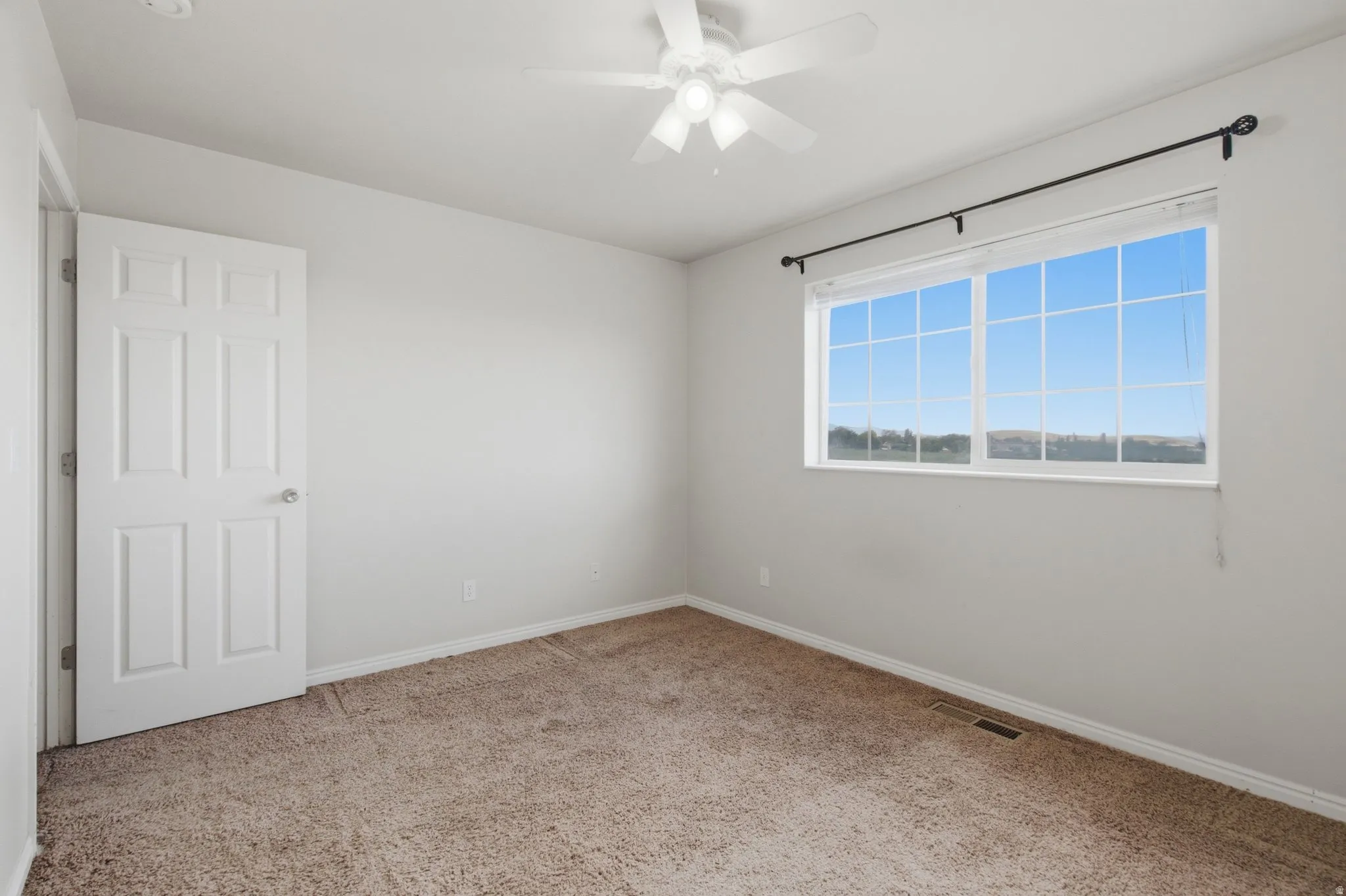 Wall-to-wall carpeting, white interior door, ceiling fan with light fixture, and a large window with white framing
