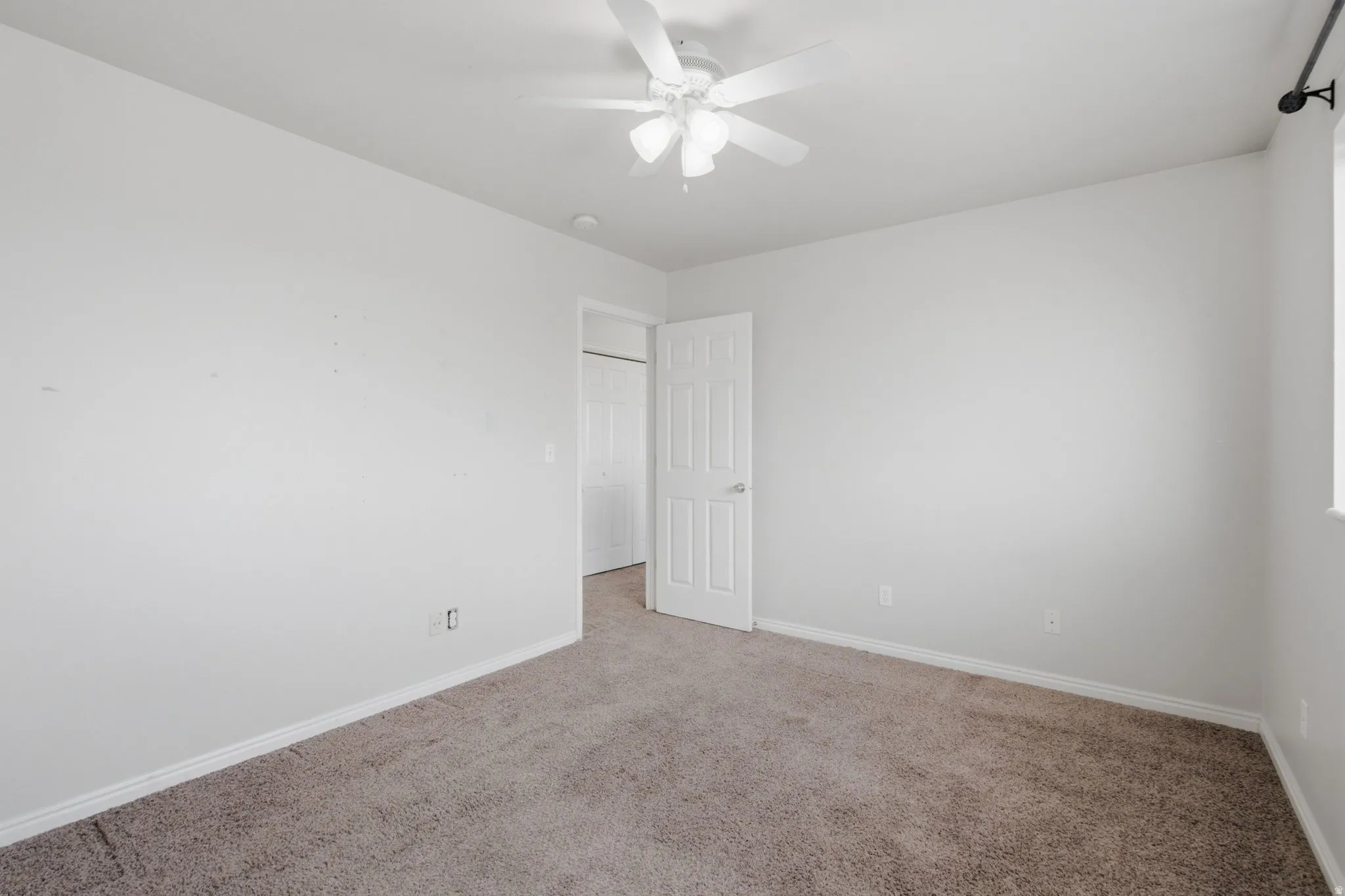 Neutral color palette throughout, featuring a ceiling fan, window with curtain rod, and carpeted flooring