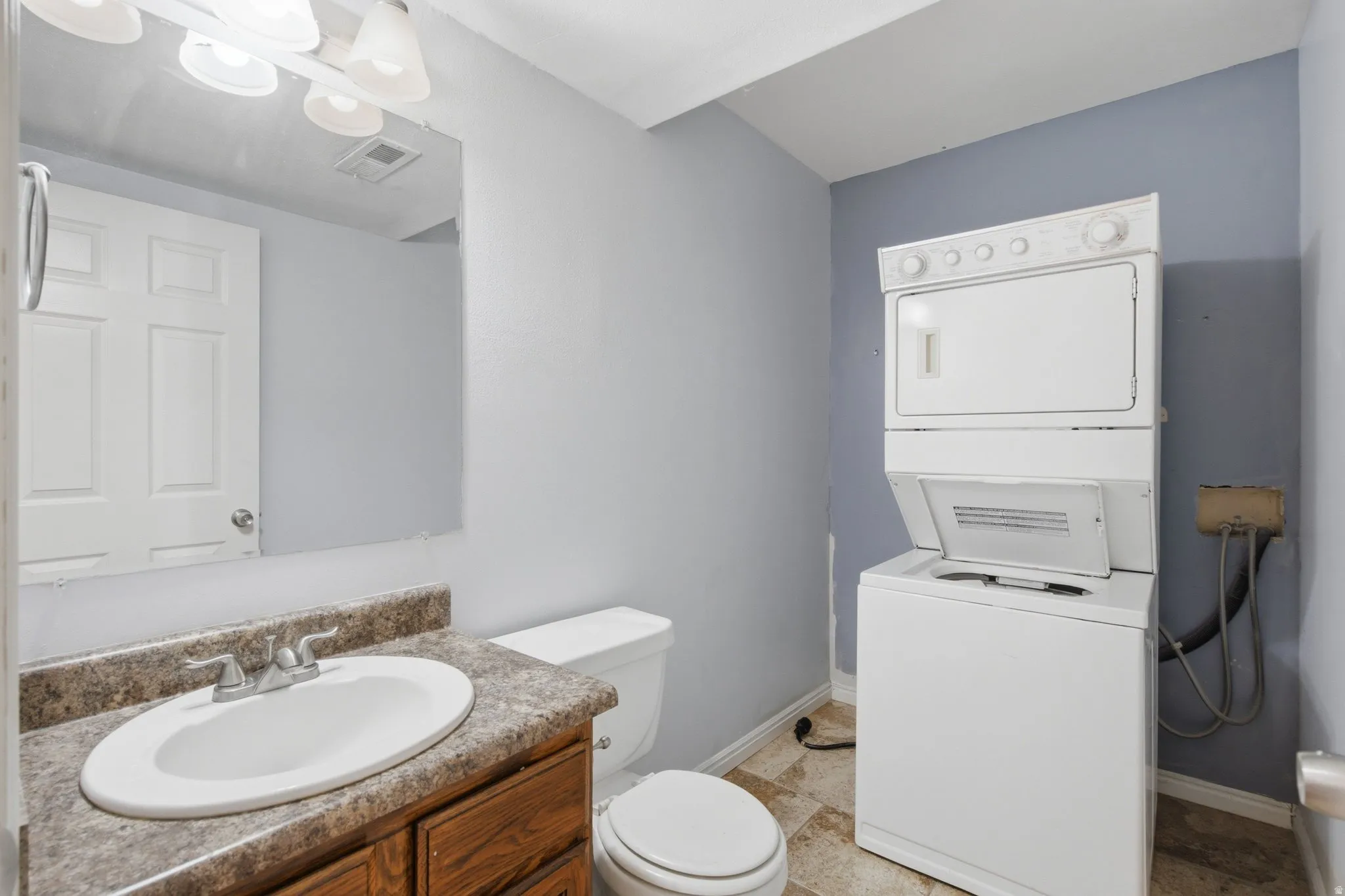 Vanity with an oval basin, a stacked washer and dryer, and a built-in mirror